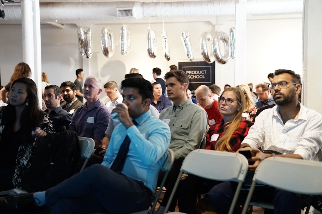 Small conference audience seated in folding chairs with name badges visible at a community gathering